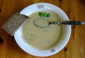 Ein Teller Kartoffelcremesuppe mit einer halben Scheibe Vollkornbrot und Basilikum